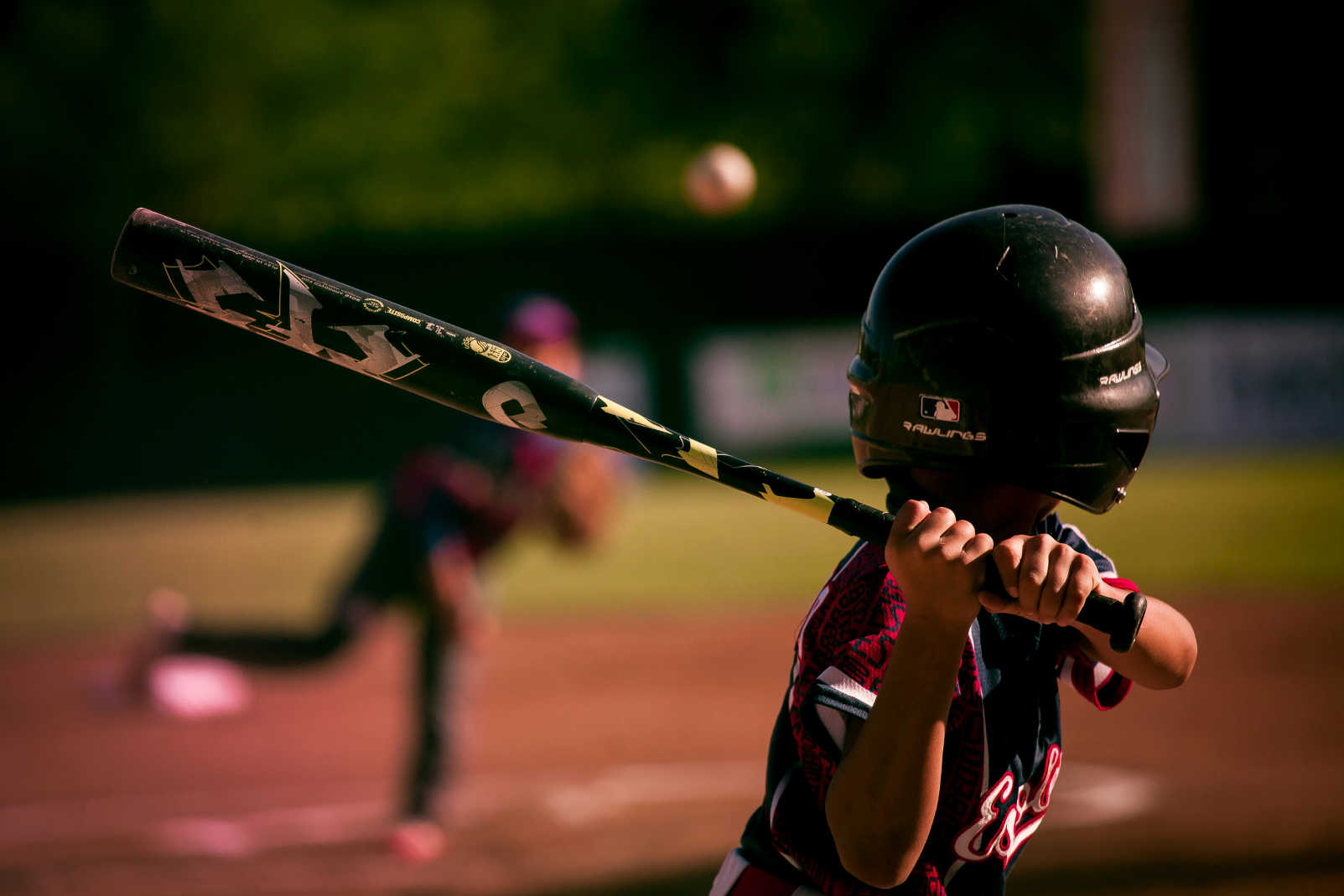 Gifts for baseball players – young athlete at bat, gripping a baseball bat, preparing to swing as the pitcher throws the ball in a sunlit game setting.