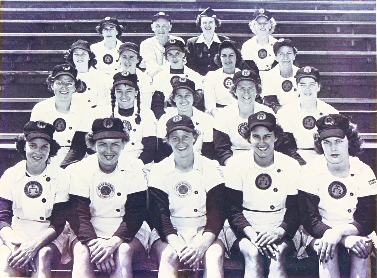 Vintage team photo of the Rockford Peaches, an all-female baseball team, wearing uniforms and sitting in stadium bleachers.
